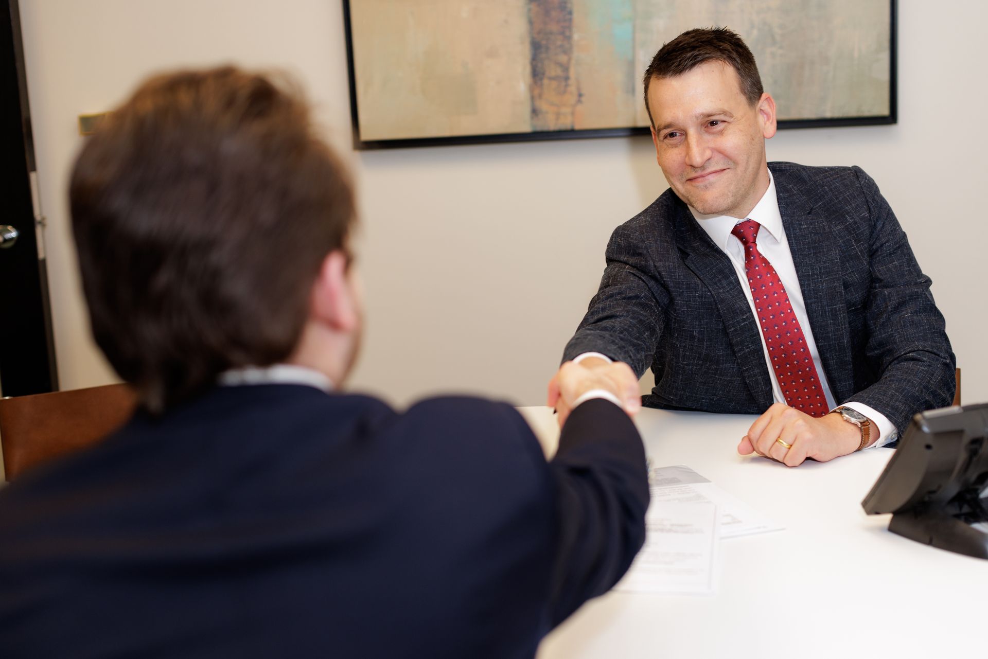 Two men are shaking hands while sitting at a table.