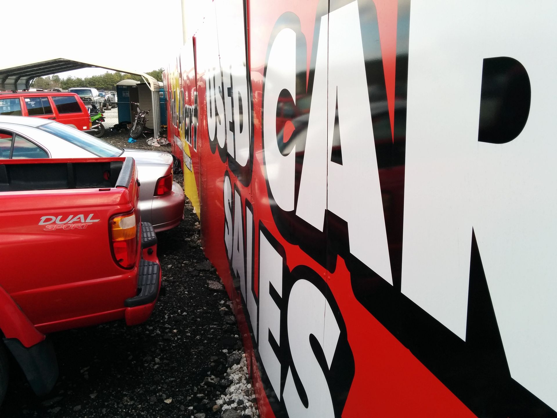 Red pickup truck parked next to a used car sales sign.
