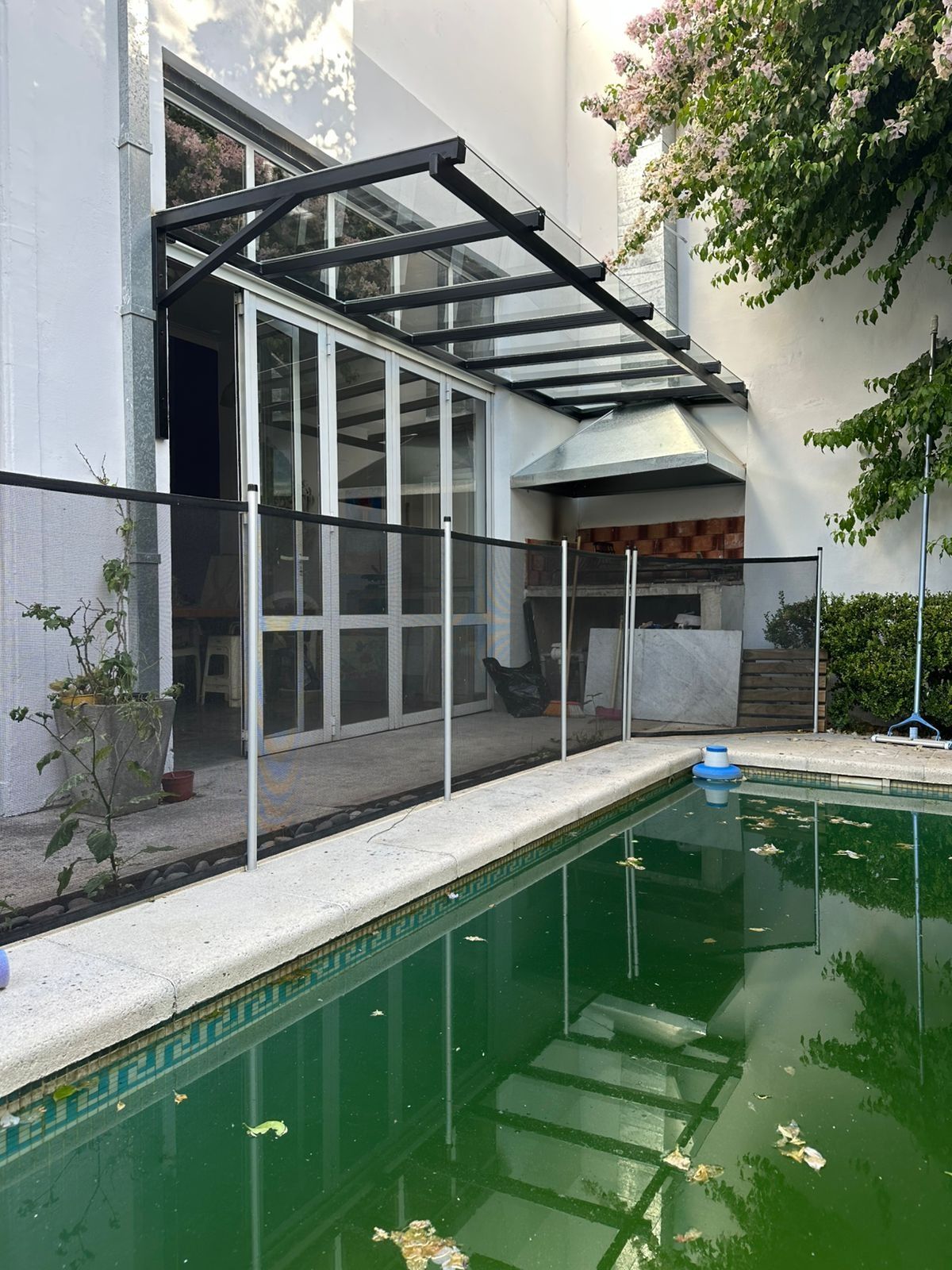 Patio moderno con marquesina de cristal junto a una estrecha piscina verde y una fachada blanca del edificio.