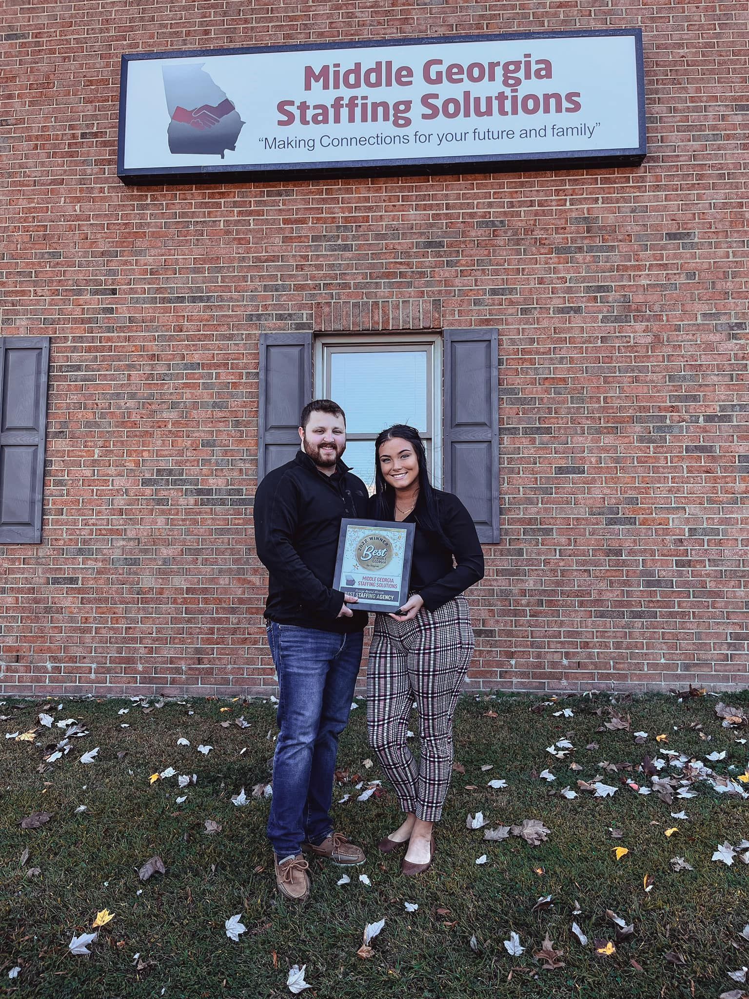 A man and a woman are standing in front of a brick building holding a plaque.