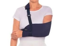 Mujer con un cabestrillo negro y una correa para el hombro sobre una camisa blanca.