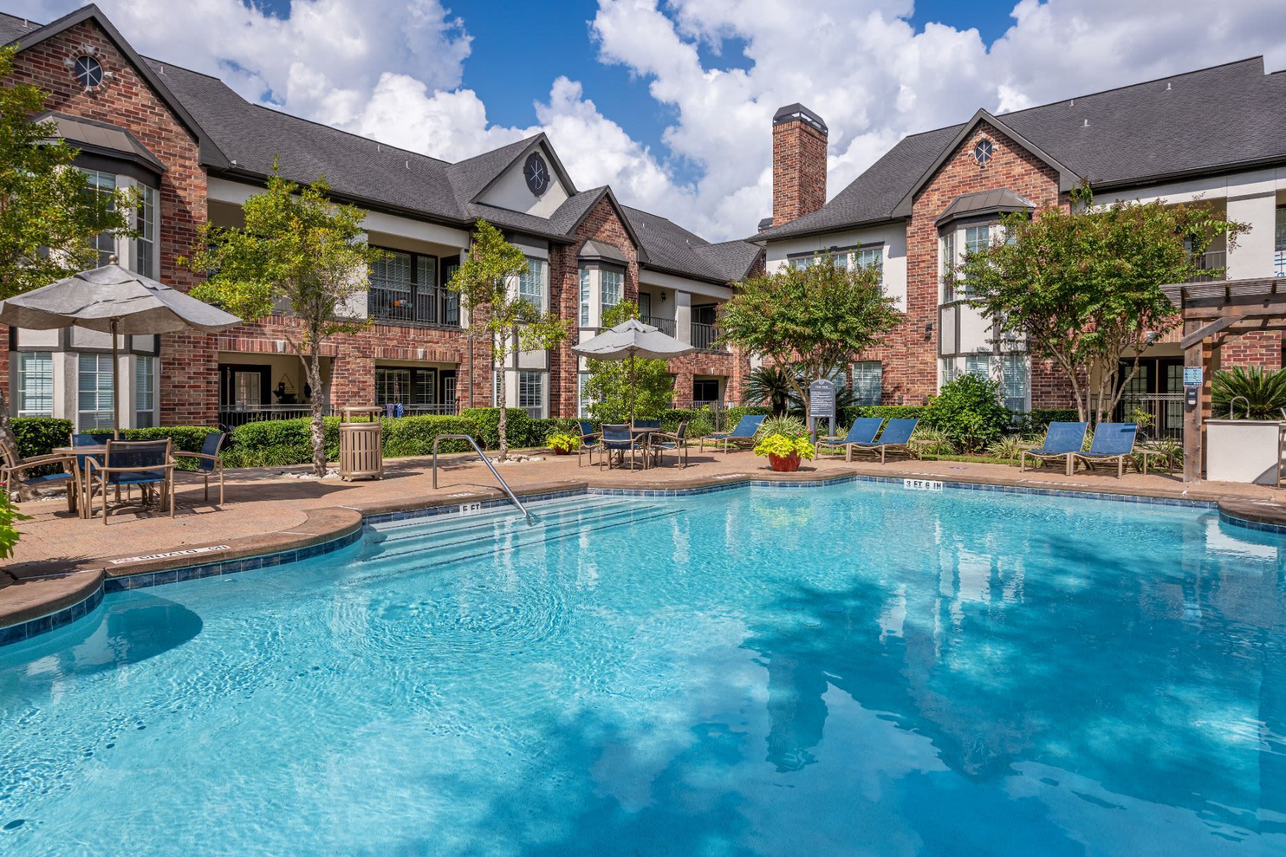 a large swimming pool surrounded by chairs and umbrellas in front of a brick building at Marquis on Memorial in Houston, TX.