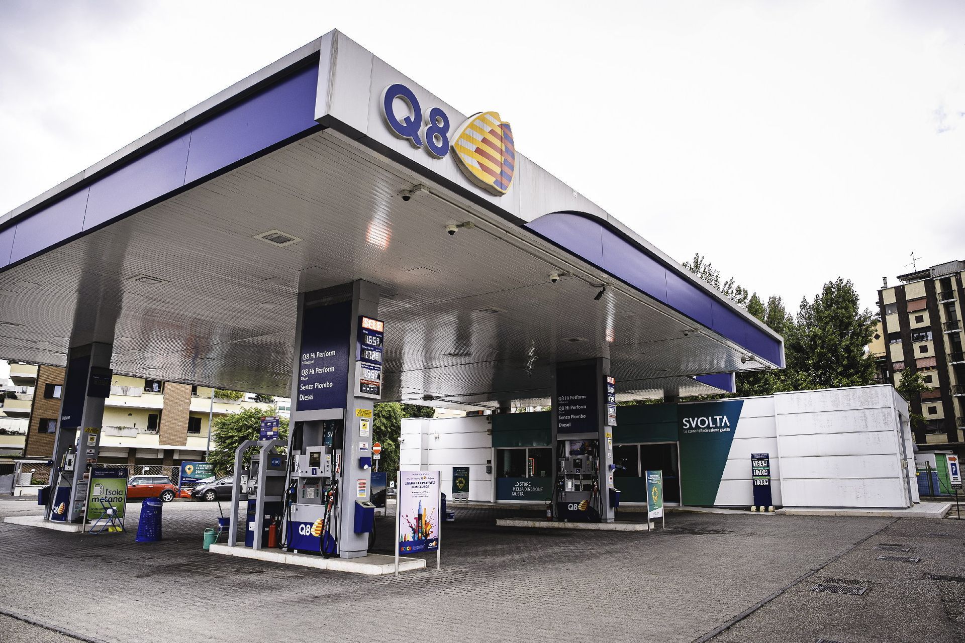 Stazione di servizio Q8 con tettoia blu e bianca, pompe di carburante visibili.