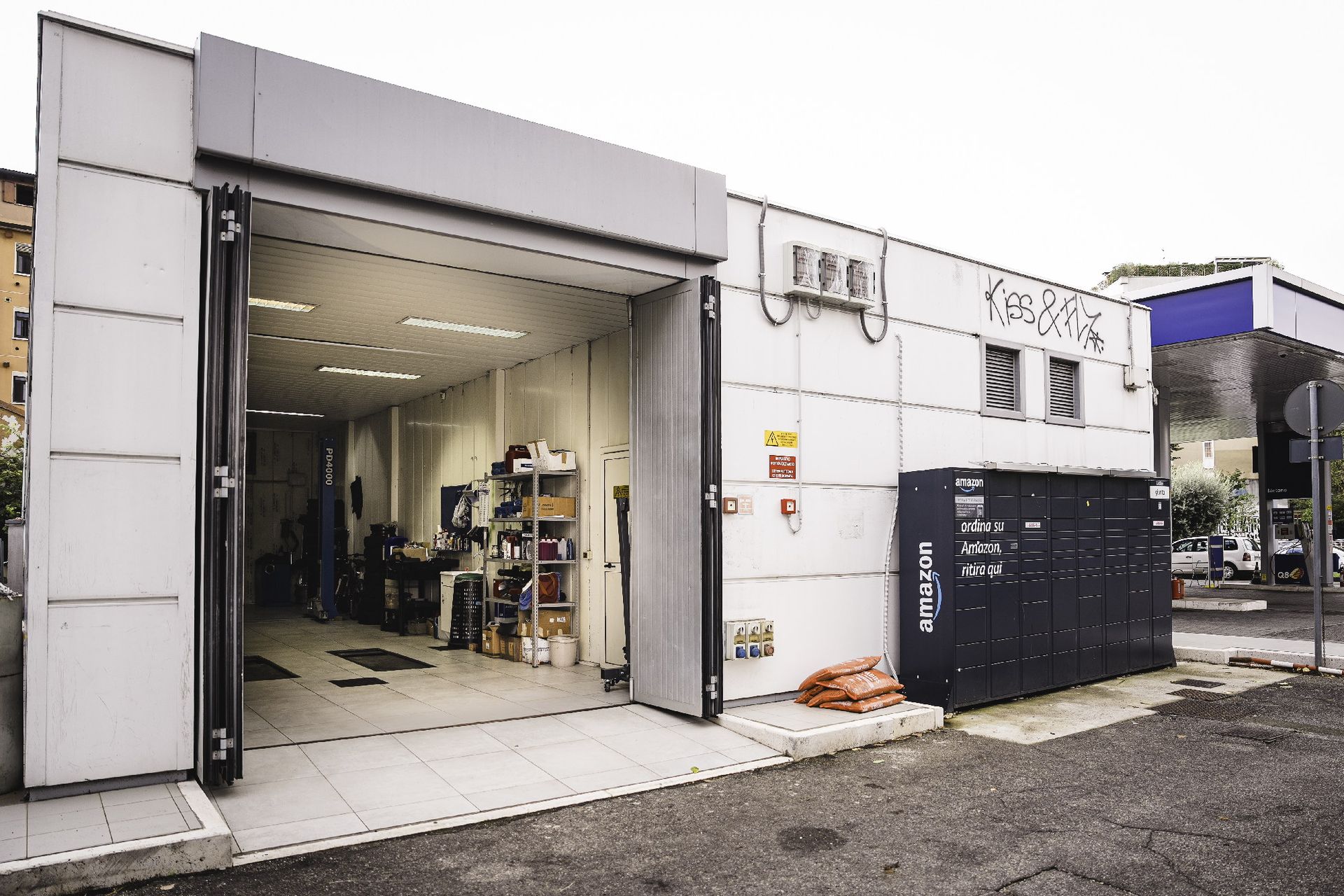 Esterno di un'officina di riparazione veicoli con porte aperte, che mette in mostra l'interno. Edificio grigio con armadietti neri.