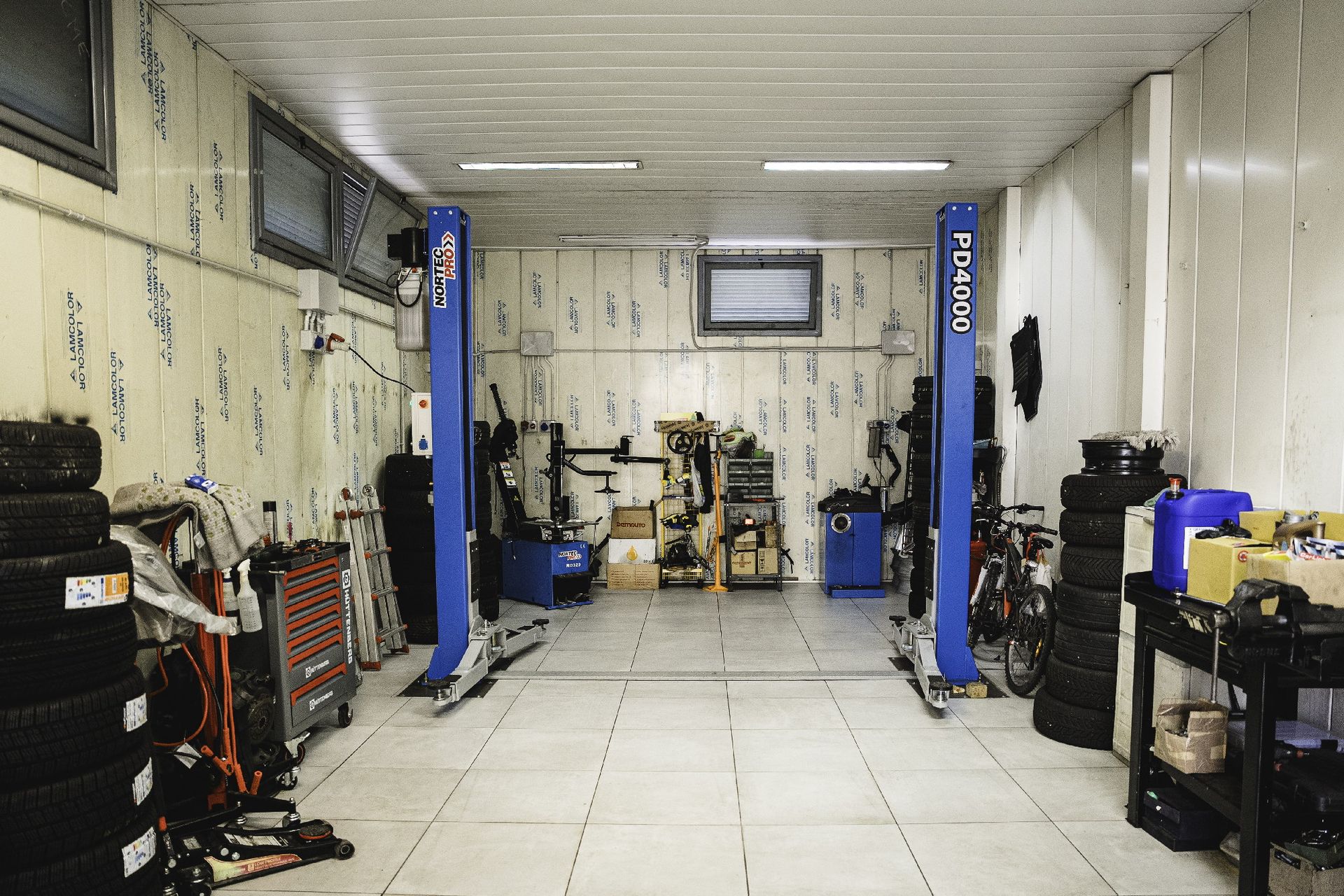 L'interno di un'officina di riparazione auto con ponte sollevatore, attrezzi e pile di pneumatici.