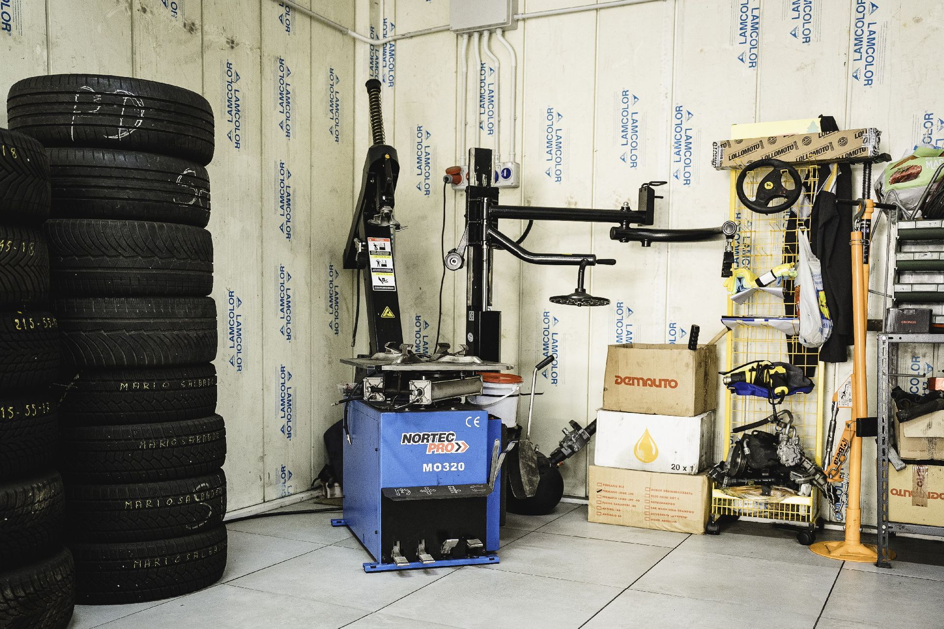 Pneumatici accatastati in un garage accanto a una macchina per il cambio gomme e vari attrezzi.