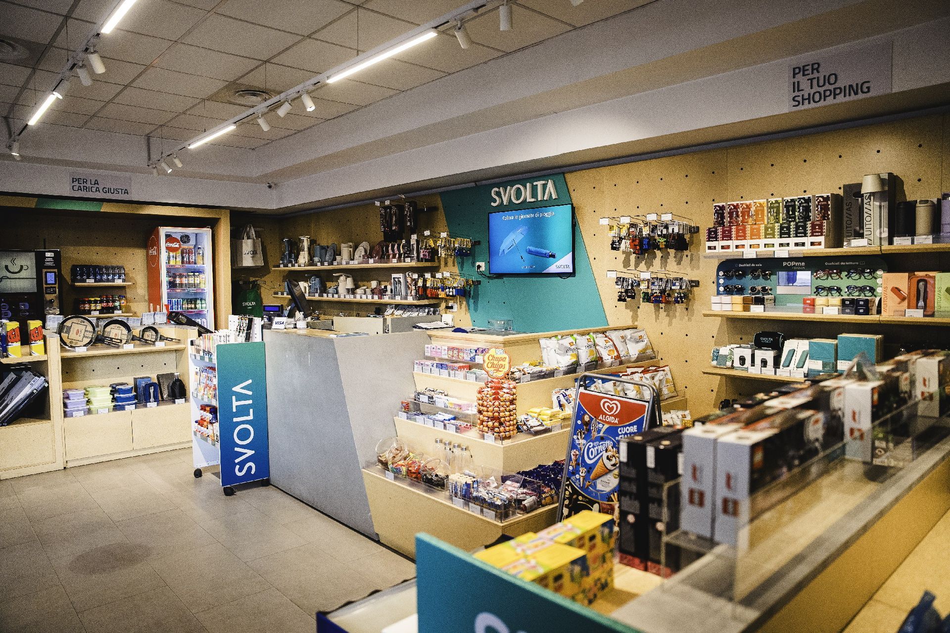 Interno di un negozio Svolta Q8 Milano, scaffali pieni di prodotti, un bancone con registratore di cassa e illuminazione dall'alto.