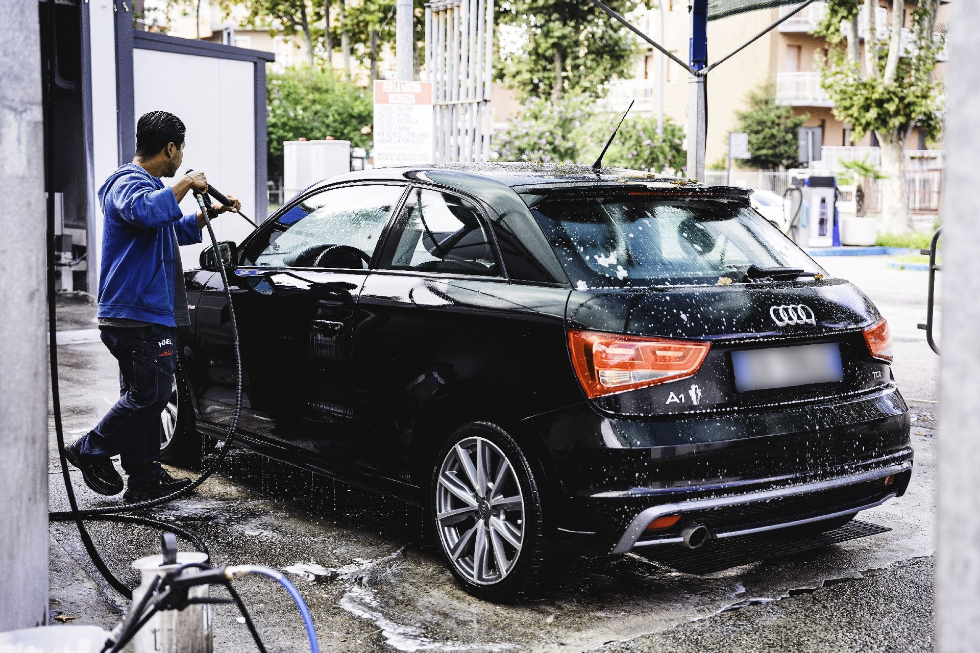 Uomo che lava un'Audi A1 nera in un autolavaggio, acqua saponata visibile, all'aperto.