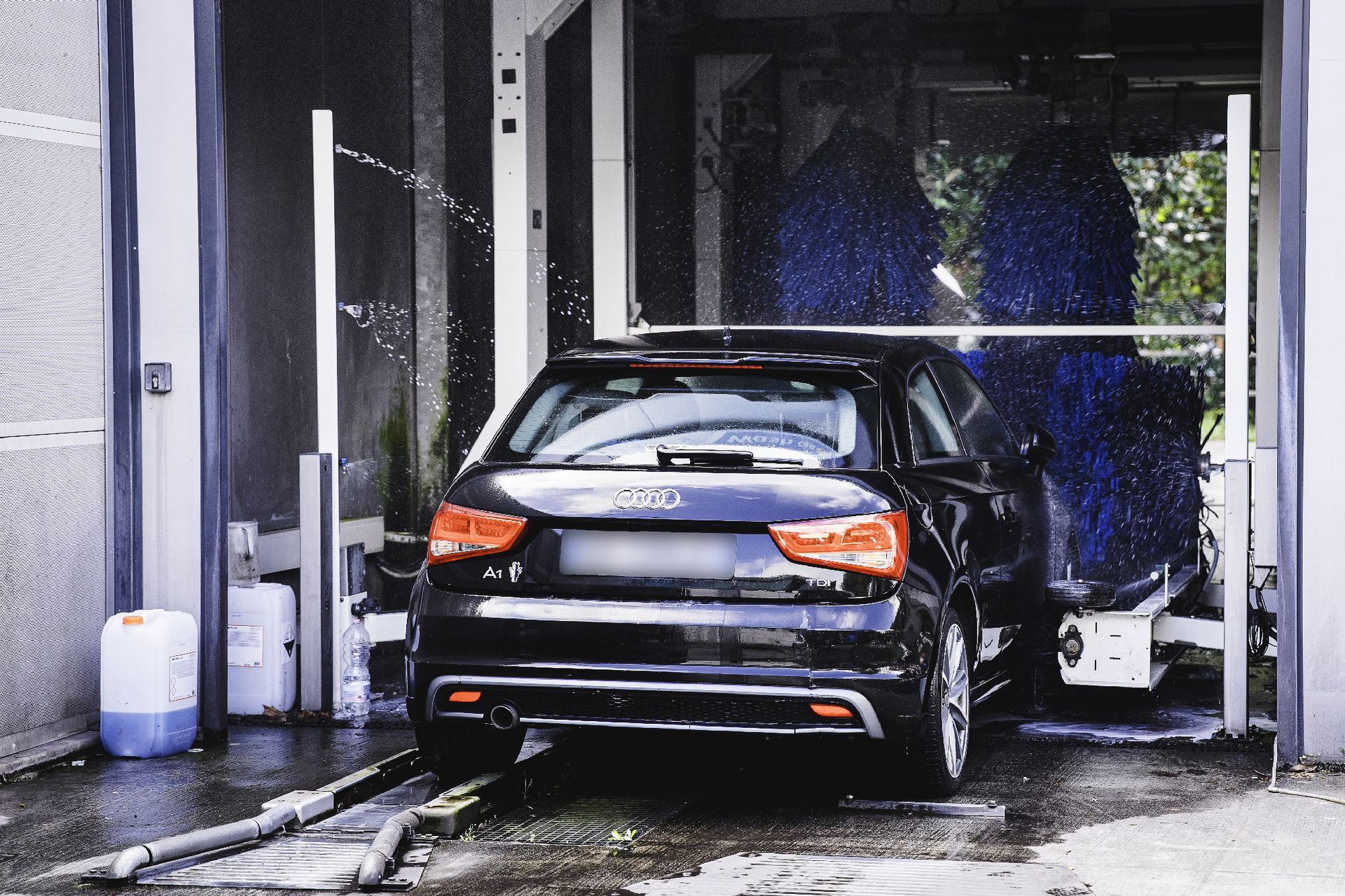 Un'auto nera in un autolavaggio automatico, spruzzata con acqua e spazzole.