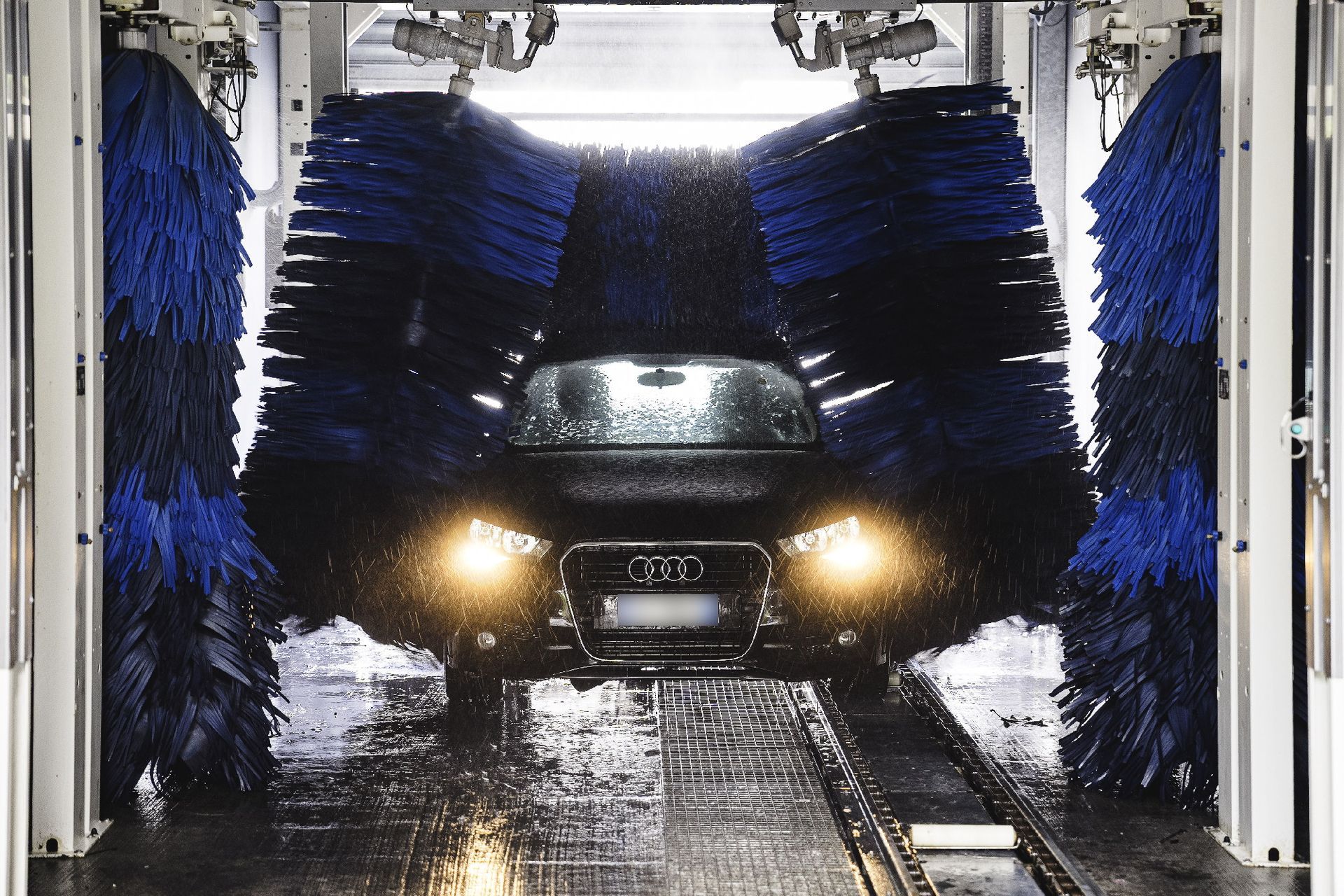 Auto lavata in un autolavaggio automatico con spazzole blu e spruzzi d'acqua.