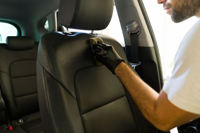 Persona che indossa guanti neri mentre pulisce un sedile nero dell'auto con una spugna.