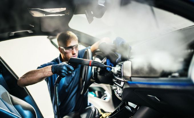 Persona che pulisce a vapore gli interni di un'auto. Indossa occhiali e guanti di sicurezza.