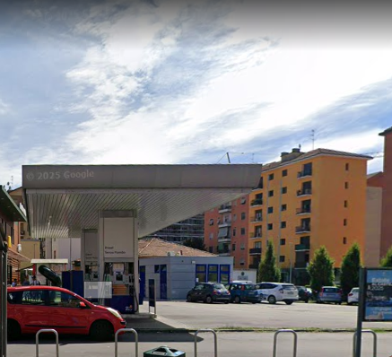 Stazione di servizio Q8 in via delle forze armate a Milanoc on un'auto rossa davanti, edifici e cielo nuvoloso sullo sfondo.