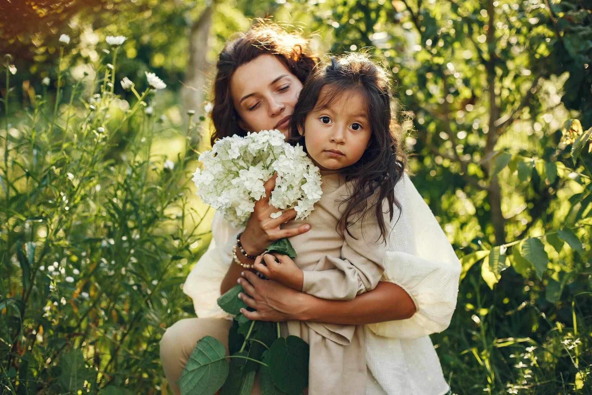 Mujer mexicana abrazando a su hija sosteniendo flores
