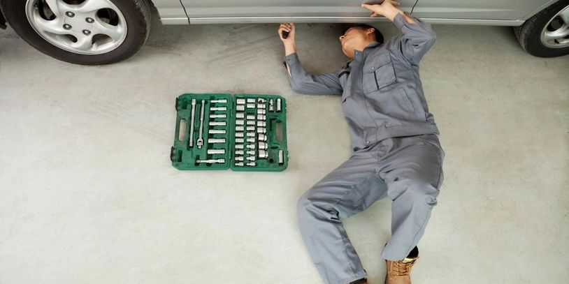A man is laying on the ground under a car in a garage. | Van Dorn Auto Repair