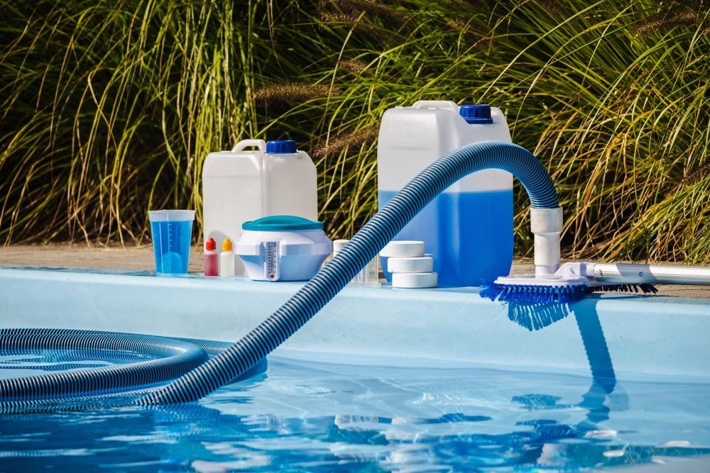 Pool cleaning supplies and hose beside a swimming pool with water running into the blue water