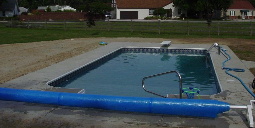 An above-ground swimming pool with a blue safety cover and metal handrails in a backyard.