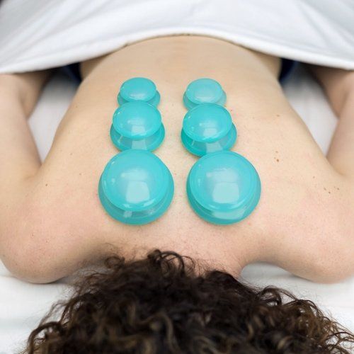 A woman is laying on a bed with blue cups on her back