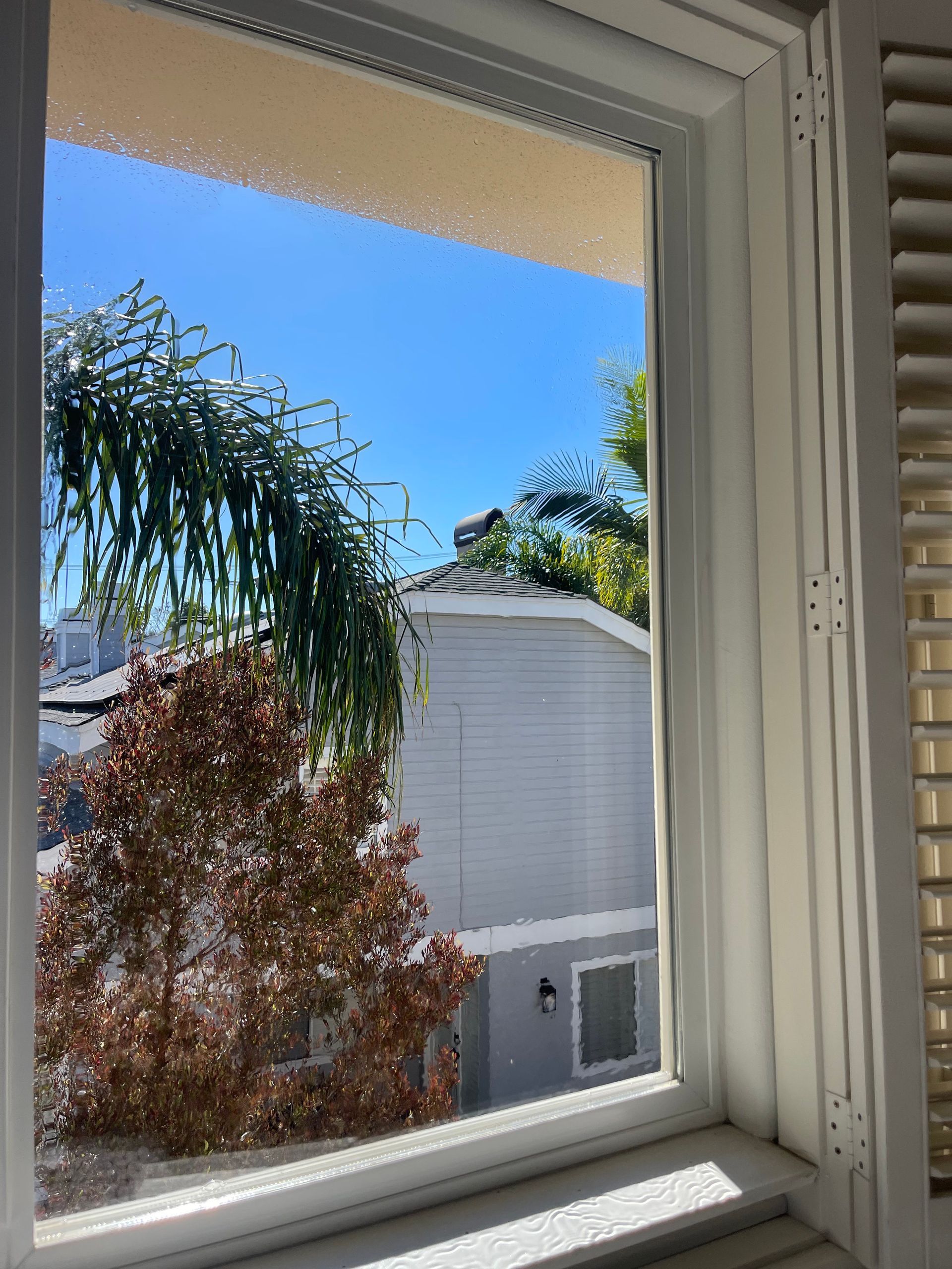 a window with shutters and a view of a house and trees