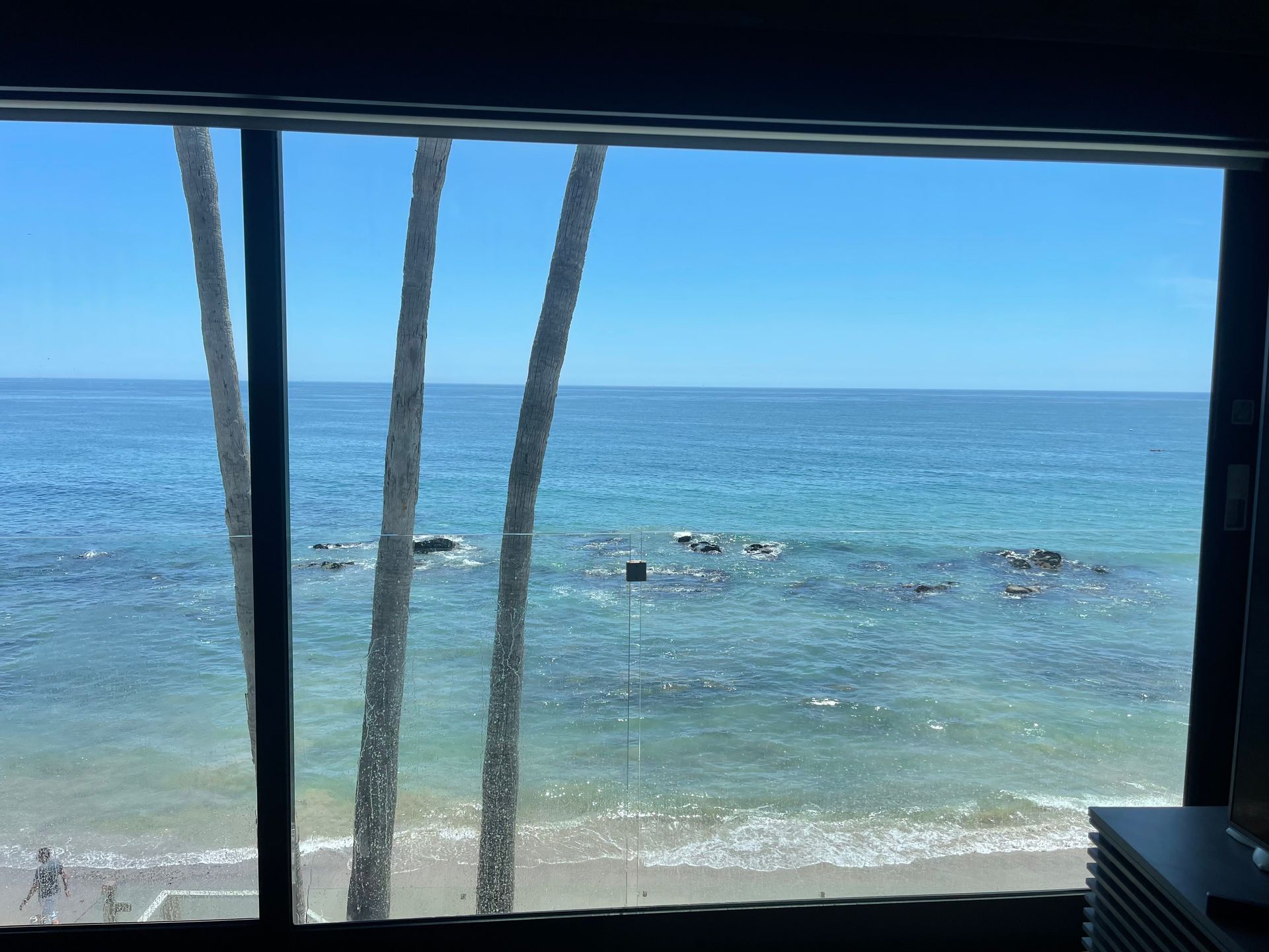 a view of the ocean from a window with palm trees in the foreground