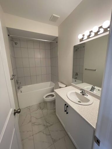 Bathroom with white fixtures, marble-look floor, and a vanity with a mirror and light fixture.