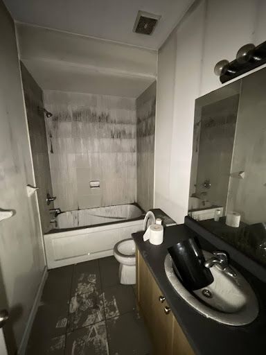 Bathroom with soot-covered walls and fixtures, showing fire damage.