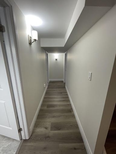 Narrow hallway with gray walls, light fixtures, and wood-look flooring.