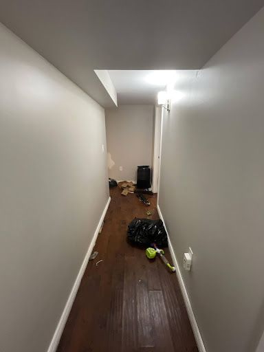 Narrow hallway with dark wood floor, debris, and gray walls; light fixtures.