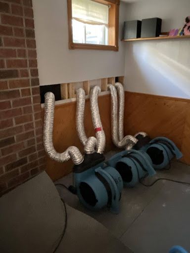 Dehumidification equipment set up in a room with a window, brick wall, and exposed wall studs.