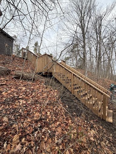 Wooden staircase ascending a wooded hillside, surrounded by brown leaves and bare trees.