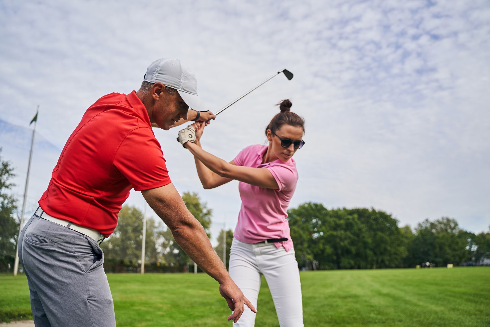 A man is teaching a woman how to swing a golf club on a golf course.
