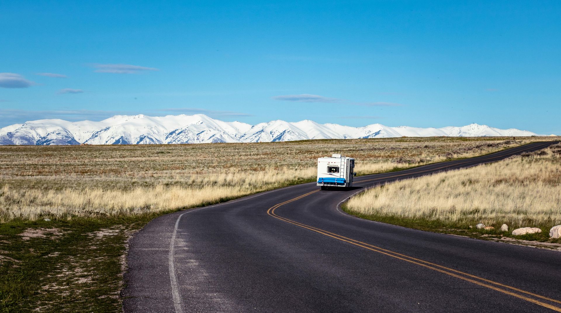 A rv is driving down a curvy road with mountains in the background.