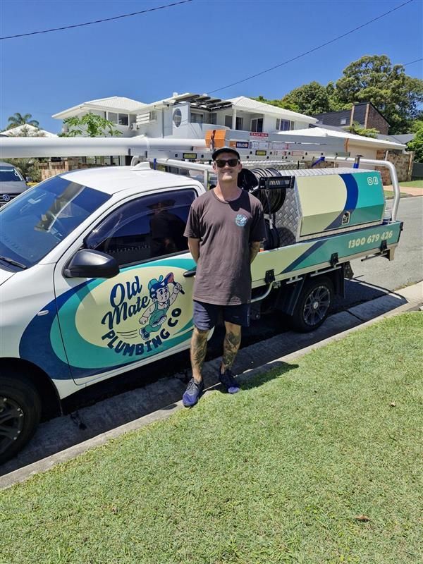 A Man In A Black Shirt Is Standing In Front Of His Work Ute — Old Mate Plumbing Co in Hollywell, QLD