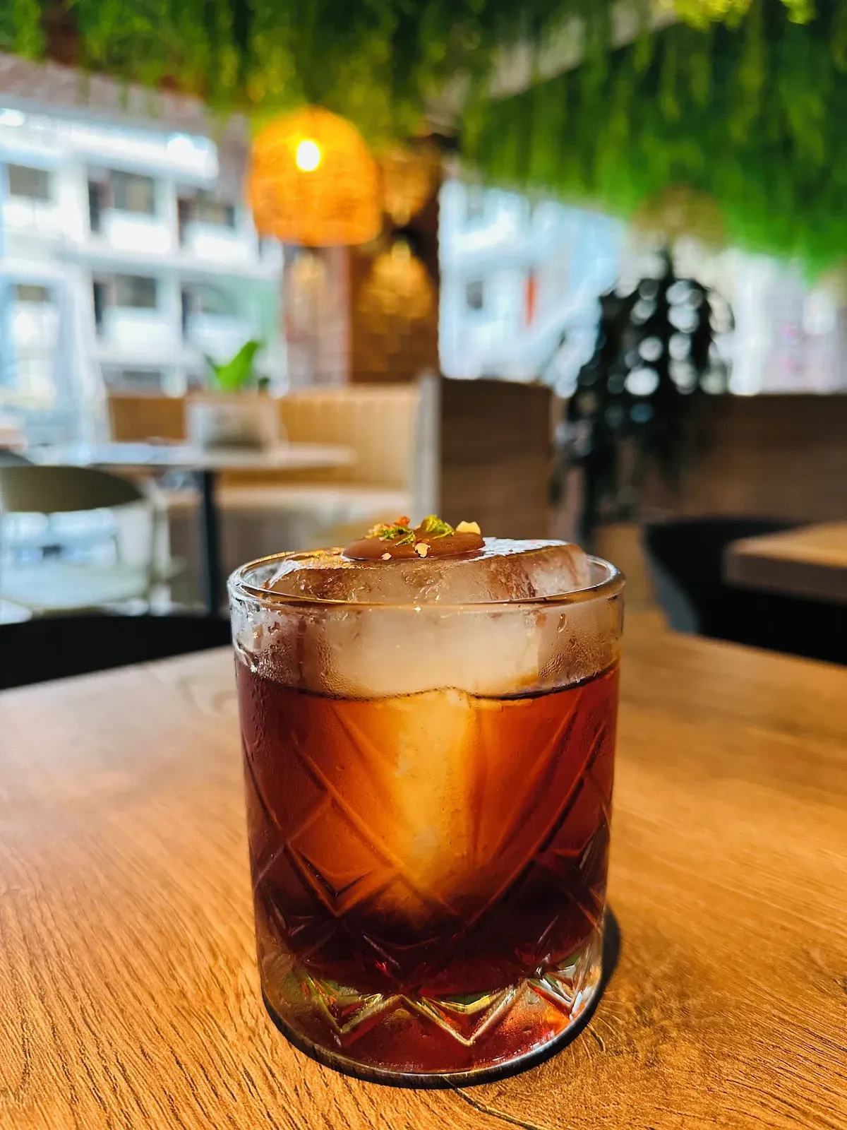 A close up of a glass of whiskey with ice on a wooden table.