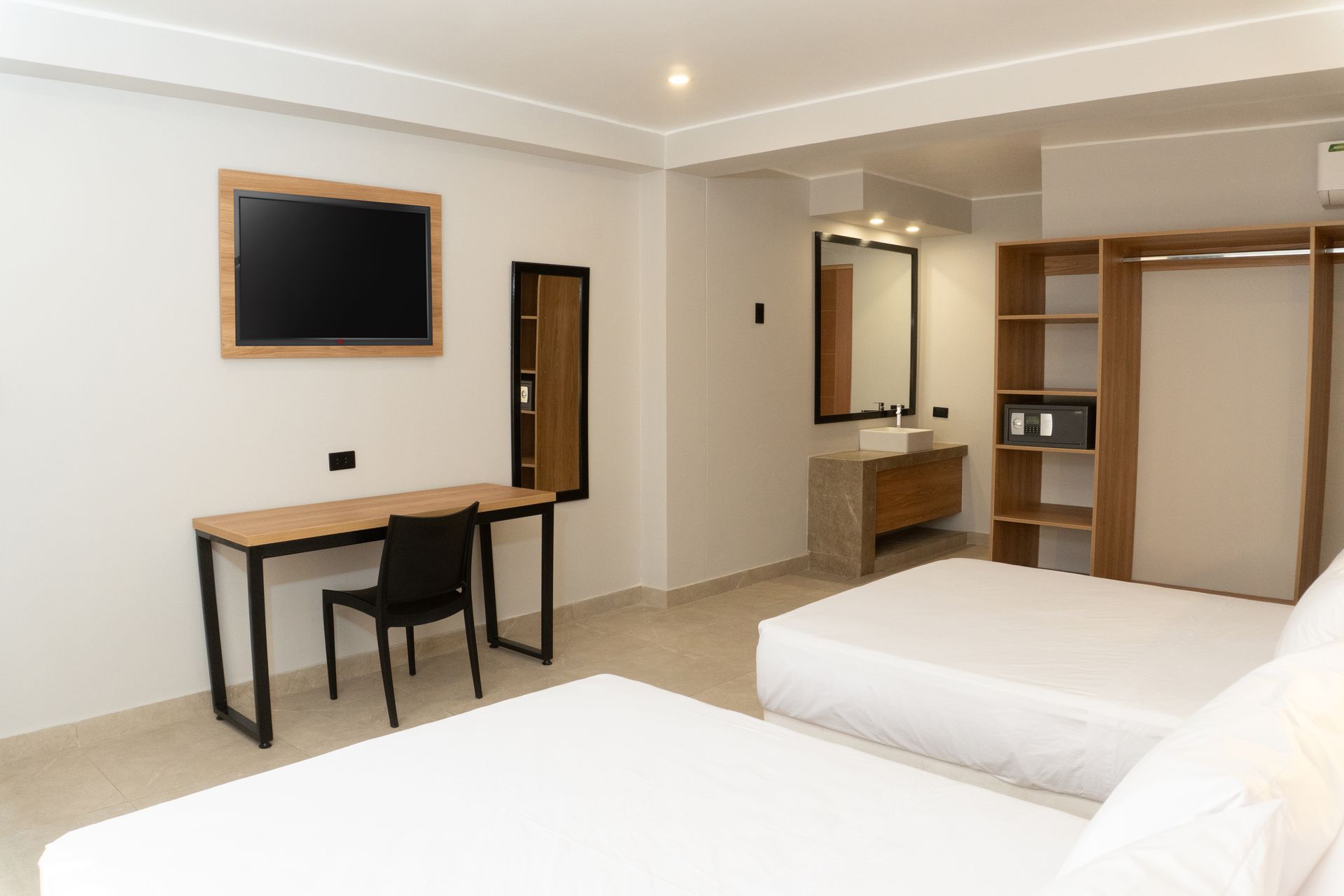 A hotel room with two beds , a desk , a television and a sink.