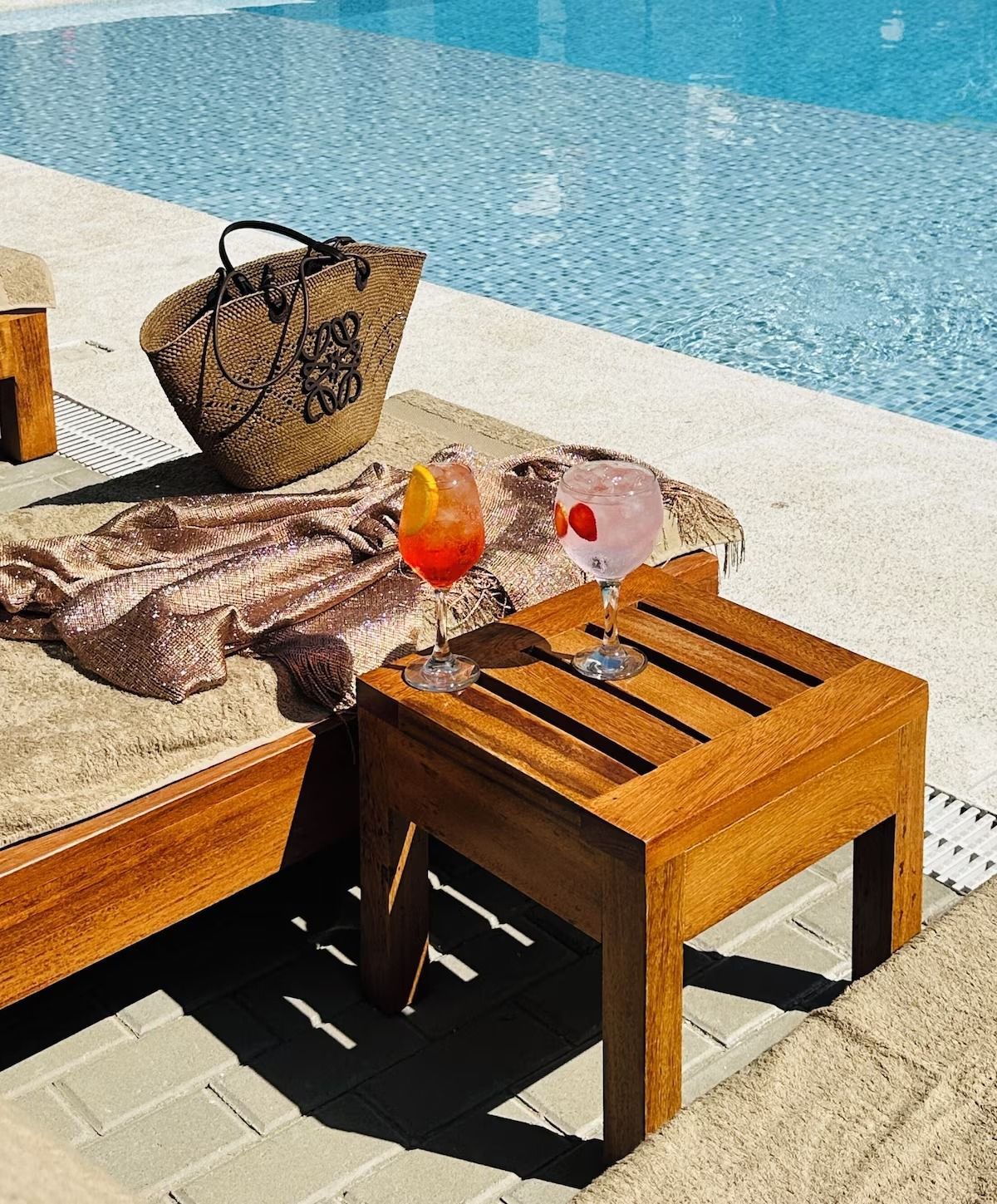 A wicker bag sits on a lounge chair near a swimming pool