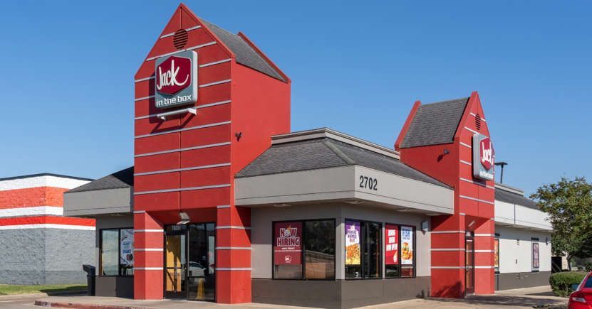 A red and white fast food restaurant with a car parked in front of it.