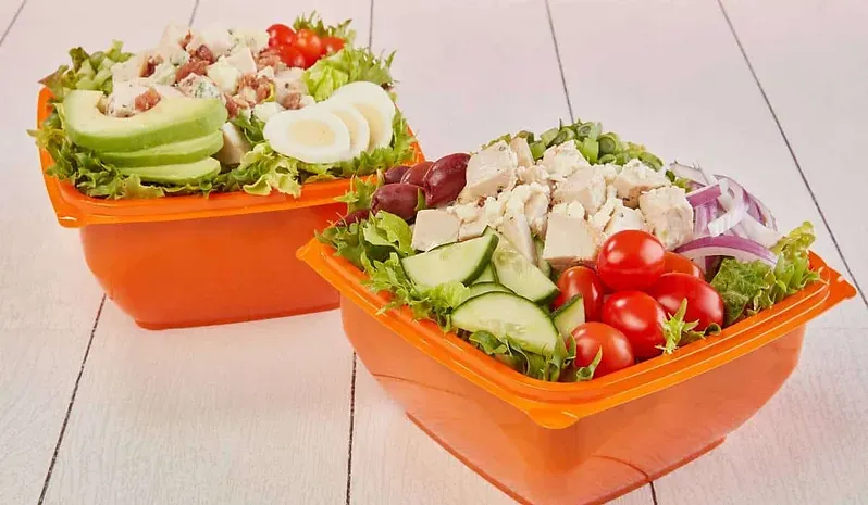Two bowls of salad are sitting on a wooden table.