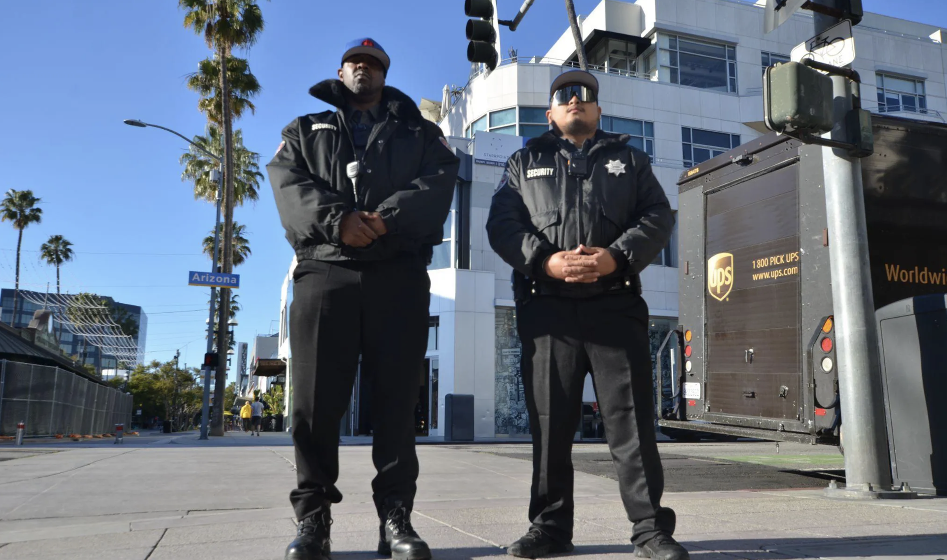 Two security guards are standing next to each other on a sidewalk in front of a ups truck.