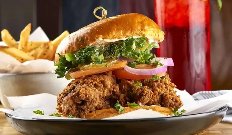A fried chicken sandwich with lettuce , tomato , onions and french fries on a plate.