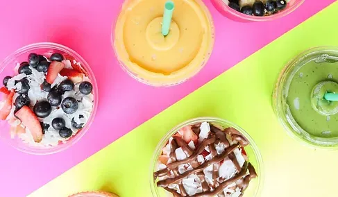 A variety of smoothies and desserts are sitting on a colorful table.