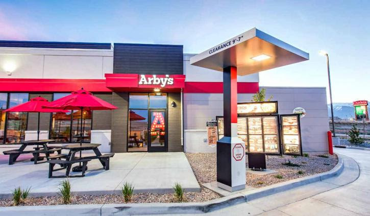 The outside of an arby 's restaurant with picnic tables and umbrellas.