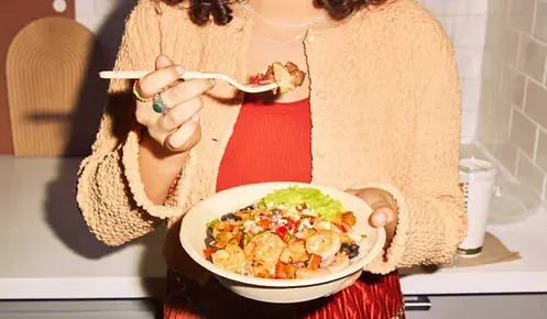 A woman is eating a bowl of food with a spoon.