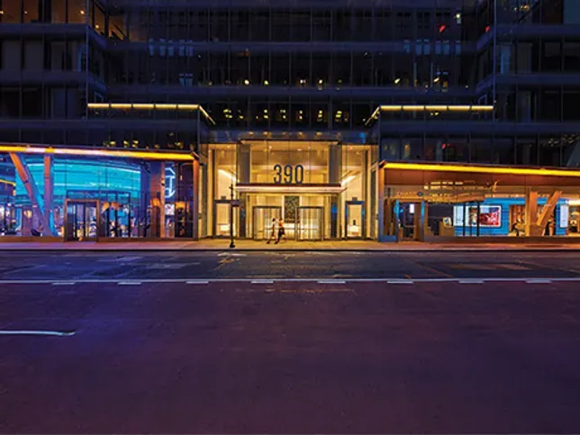 A person is walking in front of a large building at night.