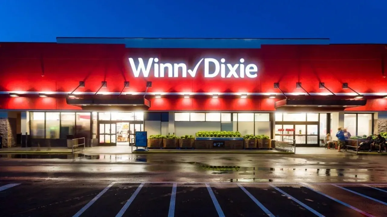 A winn dixie store is lit up at night with a parking lot in front of it.