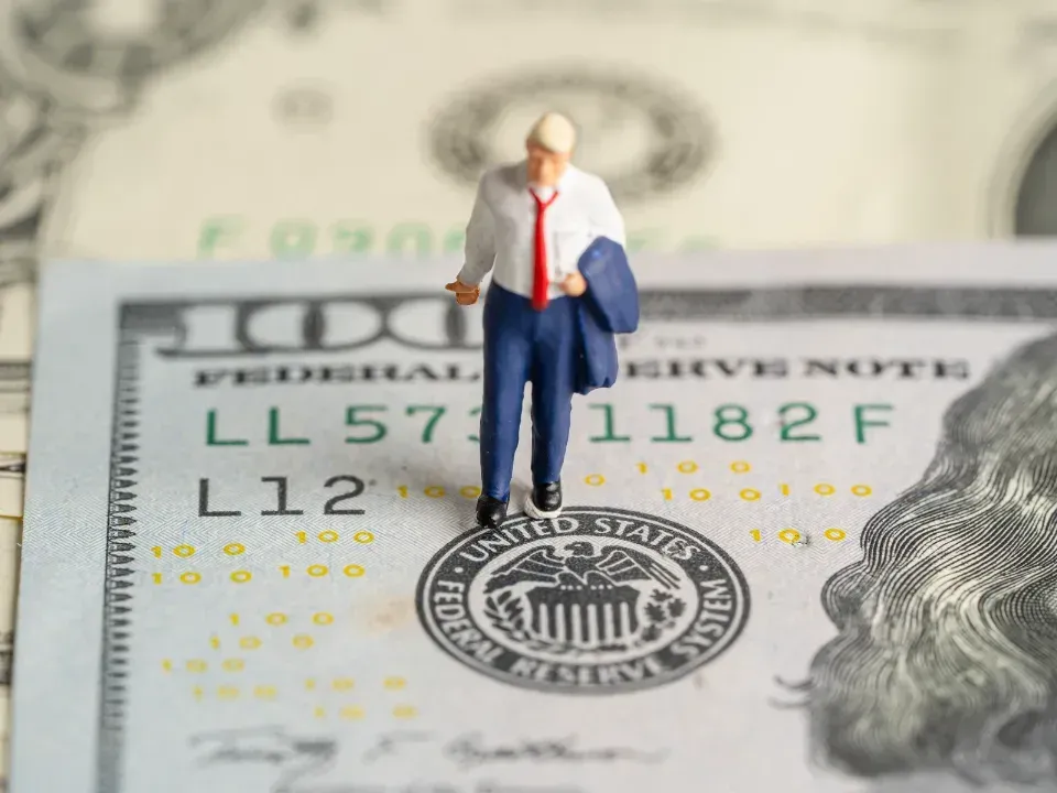 A miniature man standing on top of a 100 dollar bill