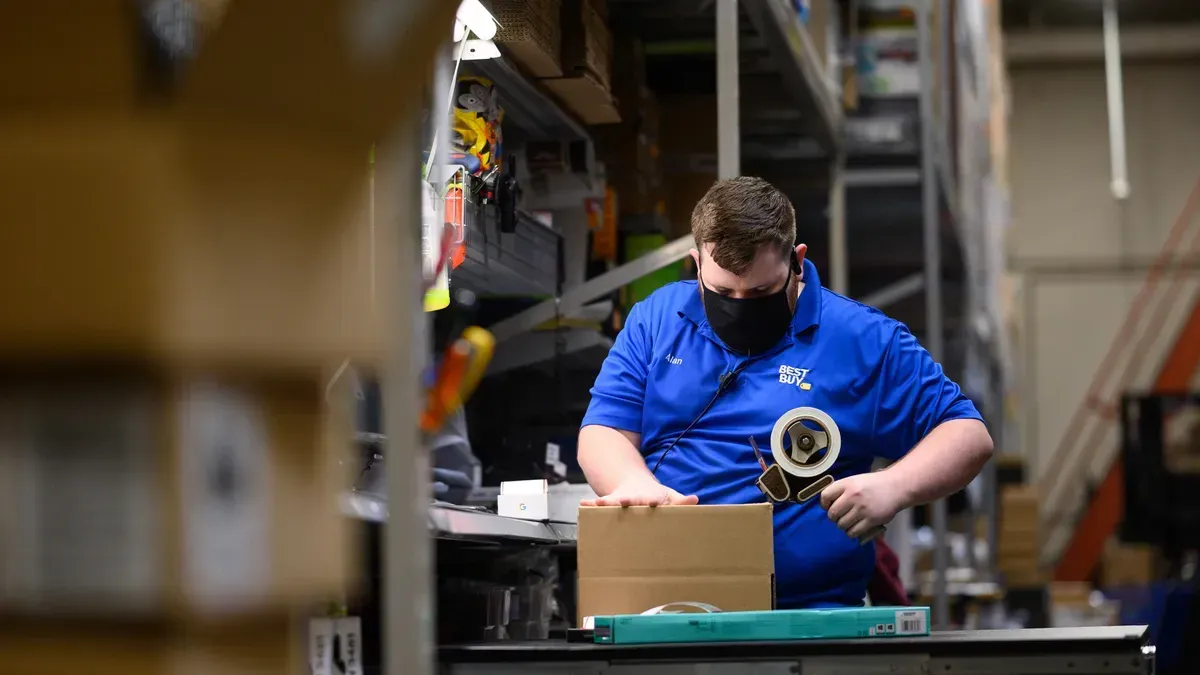 A man wearing a mask is packing a box in a warehouse.