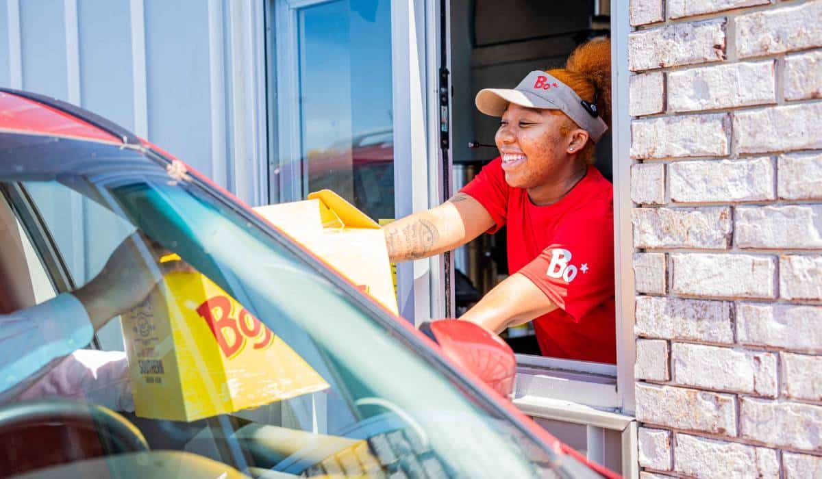 A woman is serving food to a customer through a drive thru window.