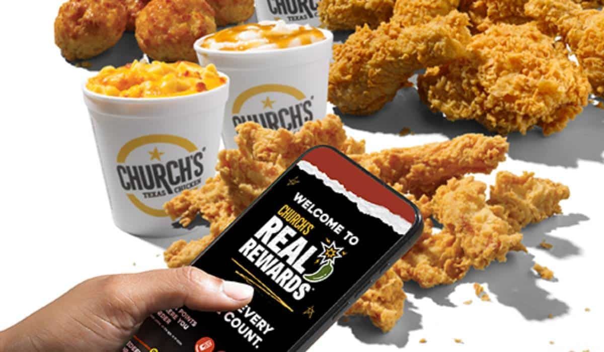 A person is holding a cell phone in front of fried chicken.