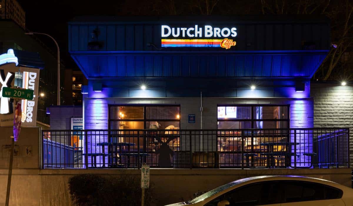 A car is parked in front of a dutch bros restaurant at night.